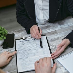An agent and clients discussing paperwork for home insurance at a meeting table.